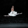 A ballerina in a white tutu split leaping.